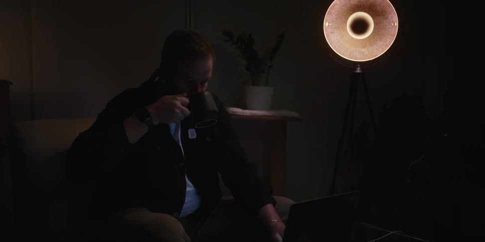 Man sitting on a couch drinking tea alone on a dimly lit room