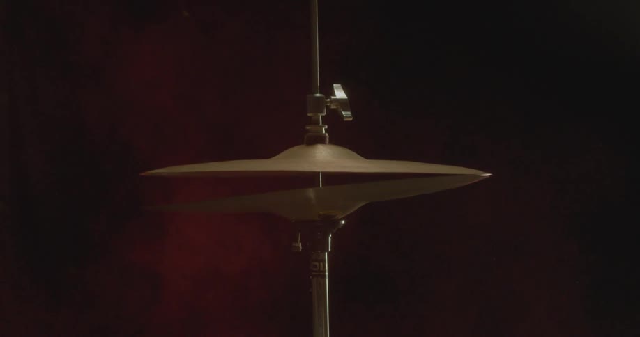 A drummer strikes a hi-hat cymbal scattering pink powder