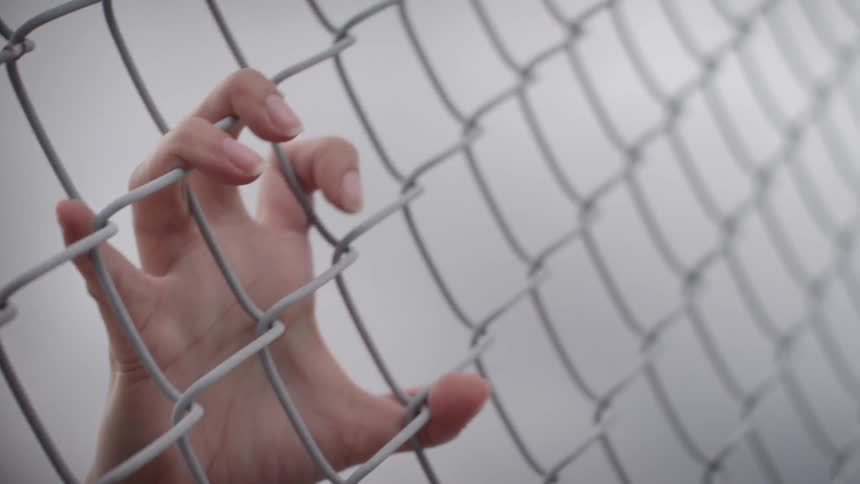 A hand reaches out and grabs a chain link fence