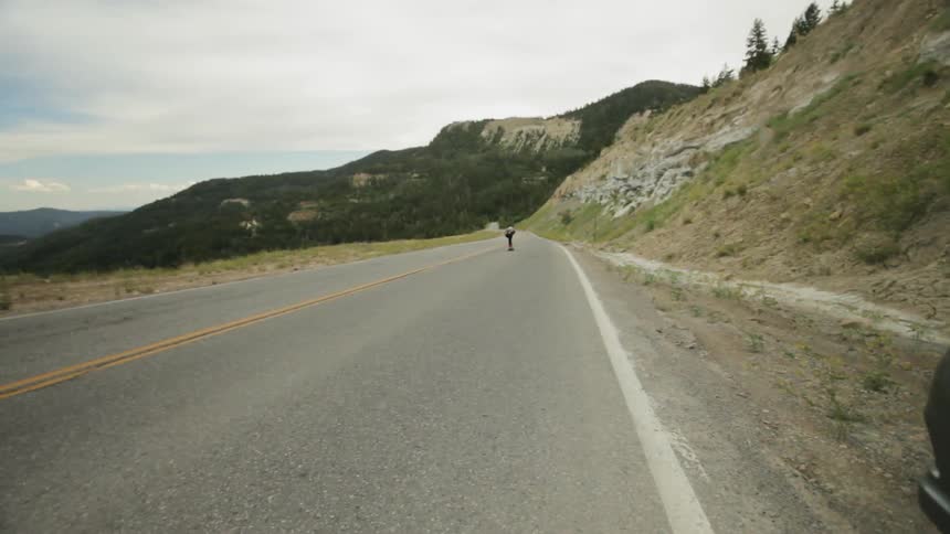 Man riding a skateboard very fast down a mountain highway