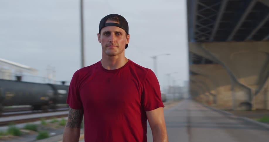 A man standing under a bridge near the train track at sunset