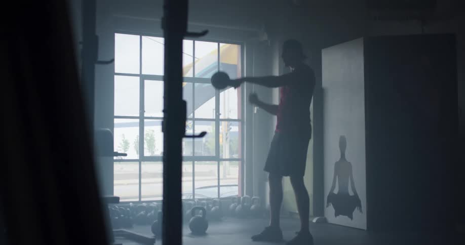 A man lifting dumbbells while standing in a dark room at midday