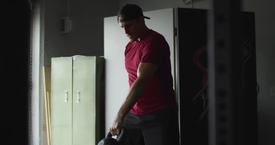 A man in a red shirt and backwards cap is lifting a dumbbell to work out his arms