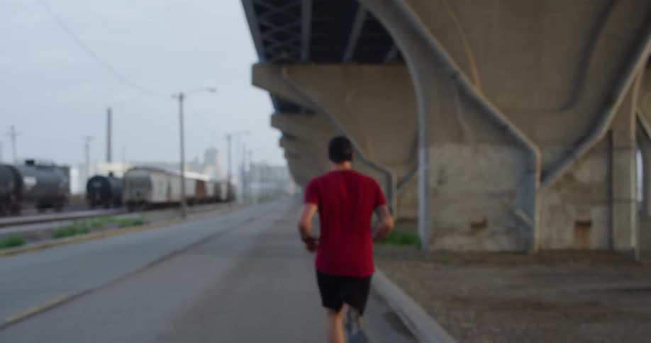 A man jugging outdoor at sunset under a bridge near a train track