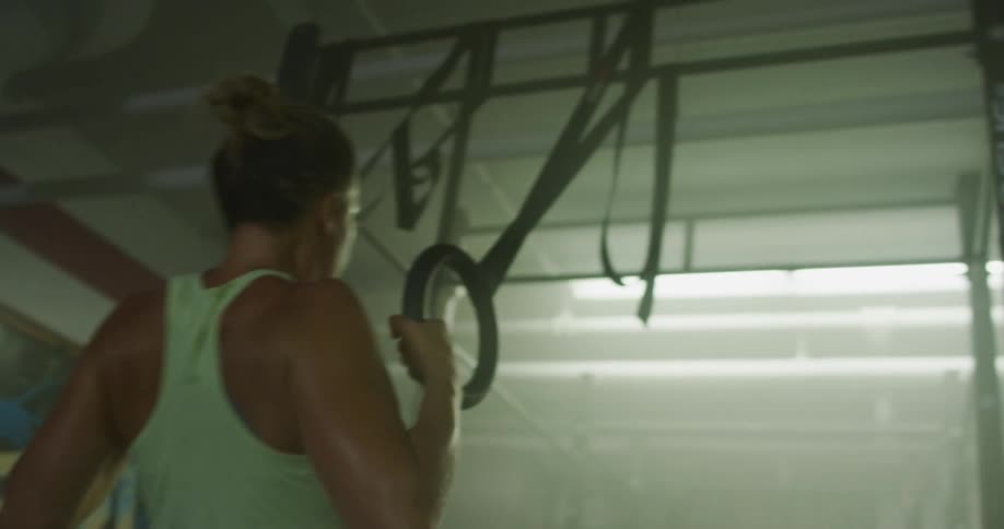 A woman lifts her body weight with metal rings and straps