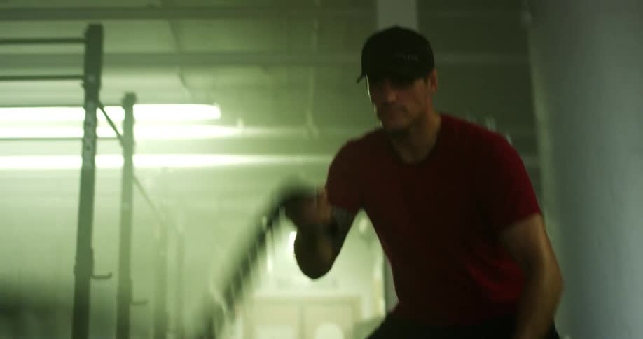 Man in a gym hitting the ropes with his arms performing cardio