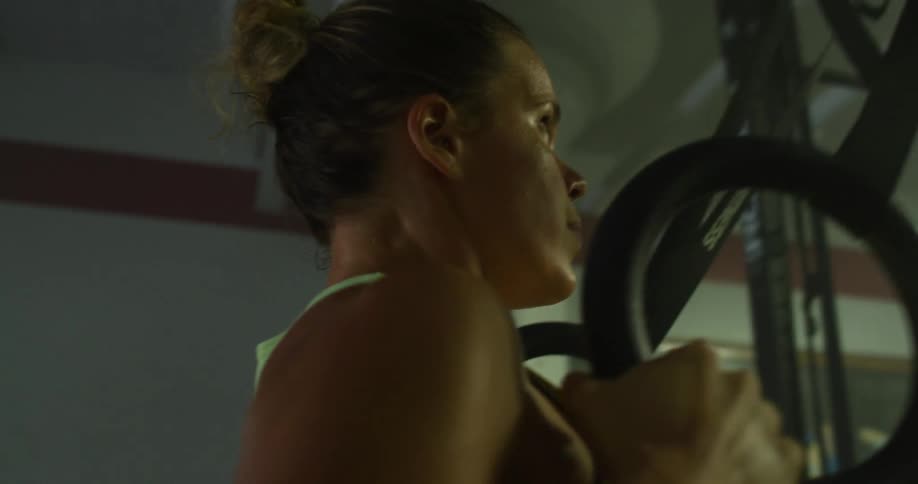 A gym scene with a woman using exercise rings