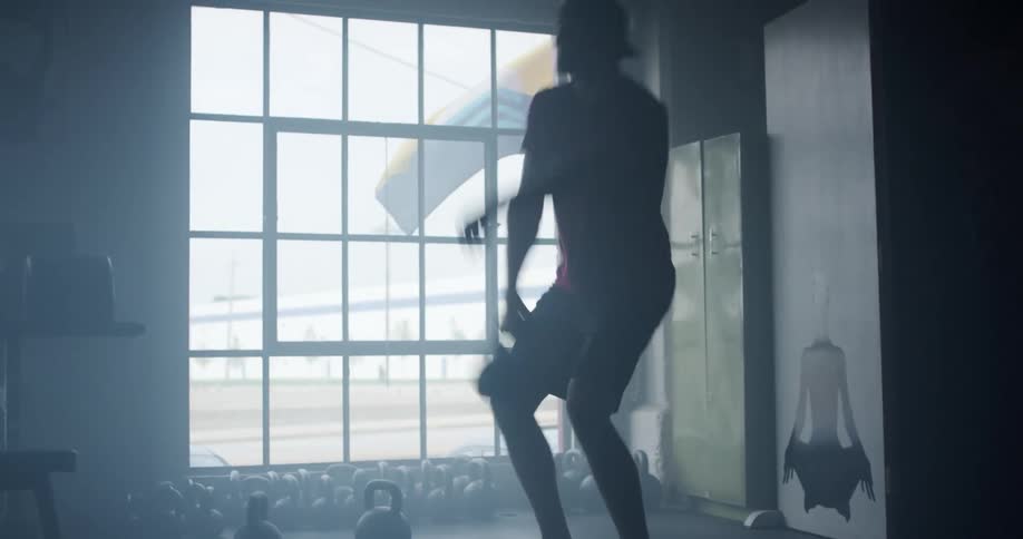 Man exercises with weights while partially silhouetted against nearby window