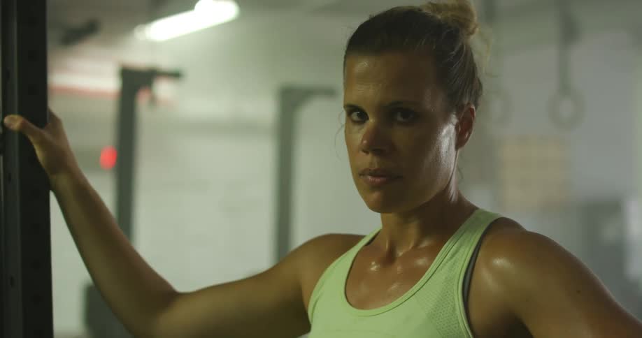 An athletic woman drenched in sweat in a gym takes a break from exercising