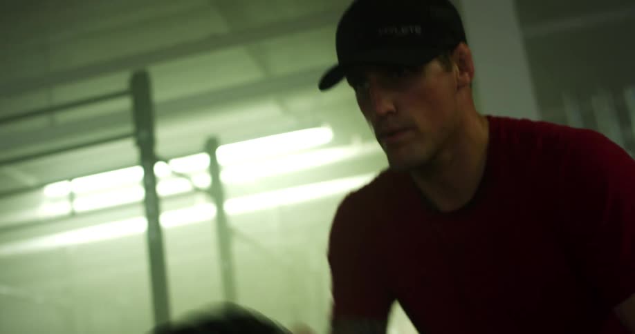 A man in a red shirt and wearing a cap is moving two ropes quickly to train his arms
