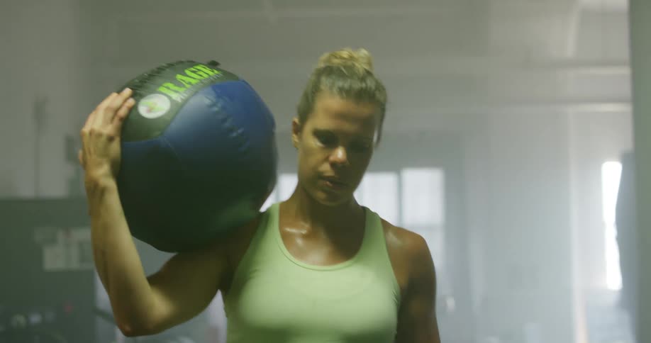 A woman picks up an exercise ball and carries it on her shoulder