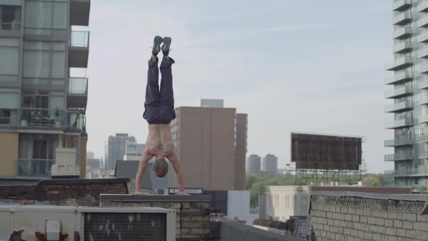 Shirtless man does handstand on a roof of a tall building