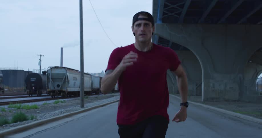 A man jogs on a road near trains and an overpass