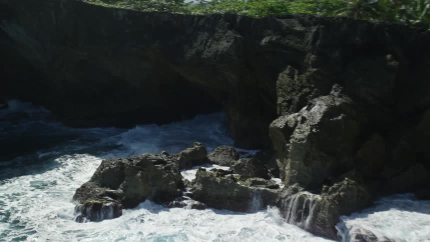 Giant waves crash into a rocky coast and move through a small cave