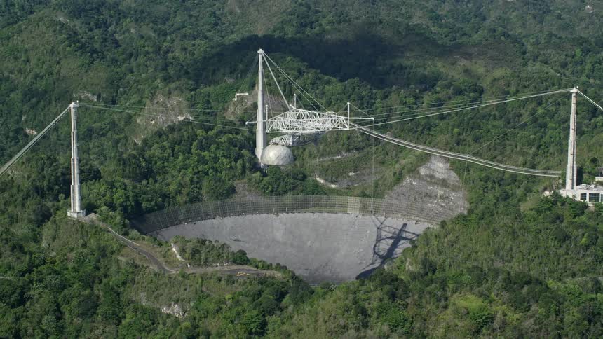 A large radio telescope sits surrounded by dense forests