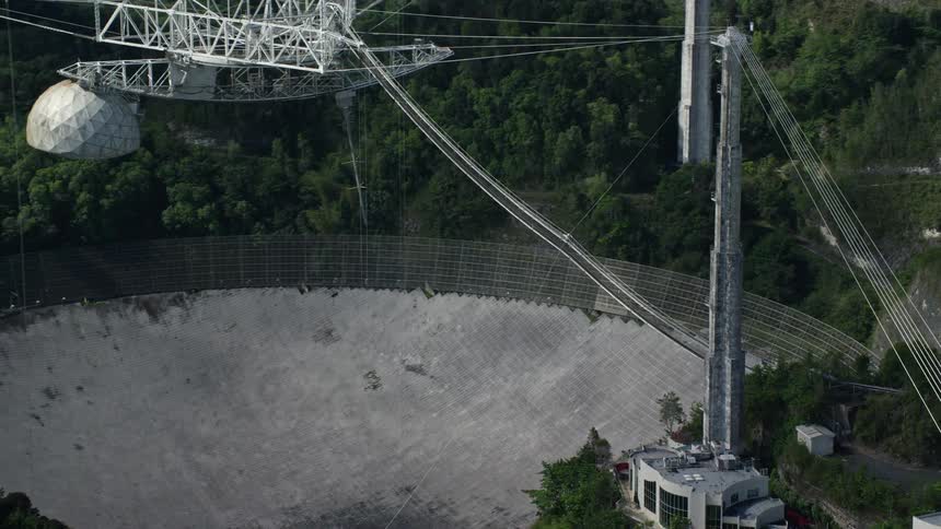 Aerial panorama of structures under a rounded rocky hole in the middle of a mountain forest