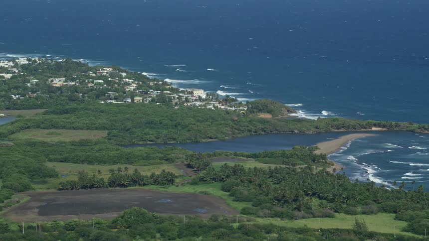 Highway parallels beach toward inlet bordered by forest near coastal town