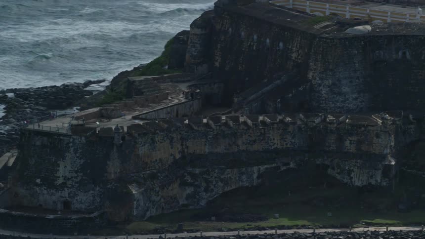 A fortress facing the sea on a coast and made of stones and with some flag