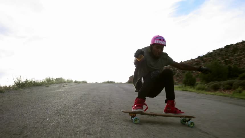 A man in a pink helmet skateboards down a hill