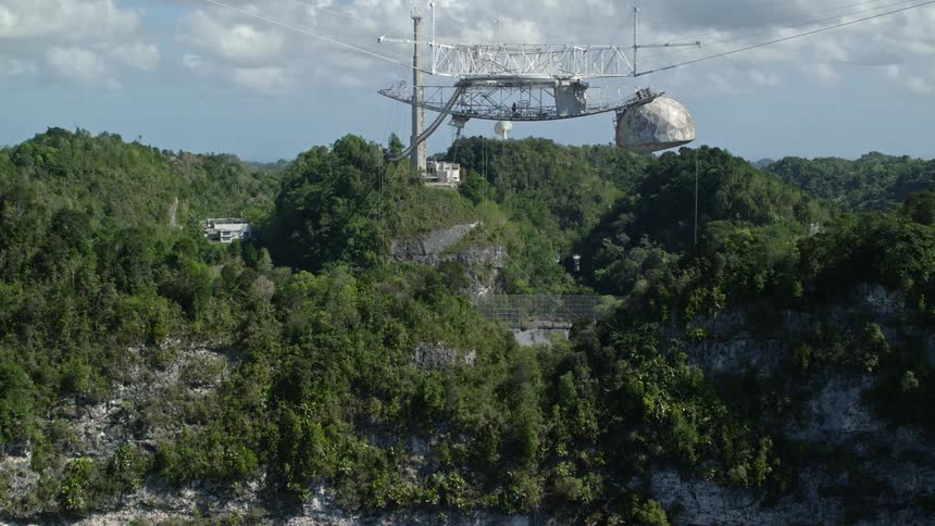 The antenna is above a large metal bowl in the mountains