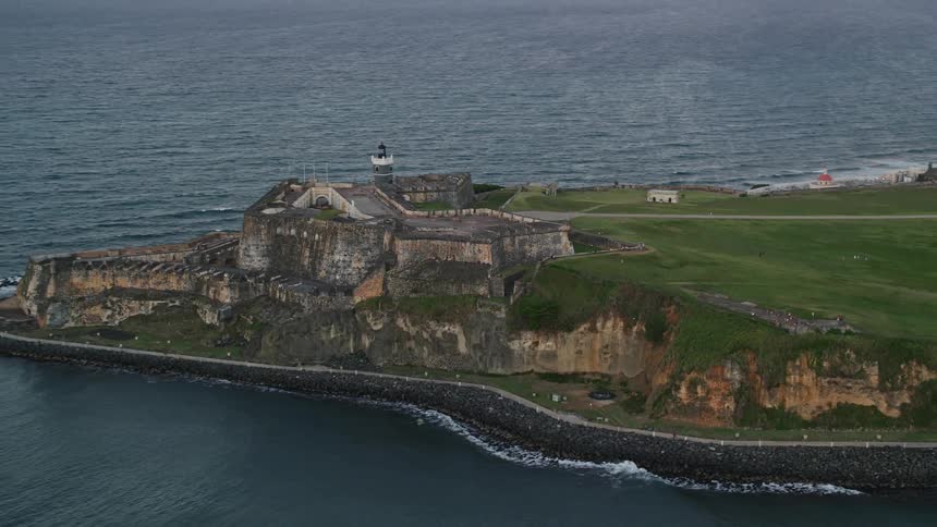 A very old stone building facing the ocean and behind a campo verde