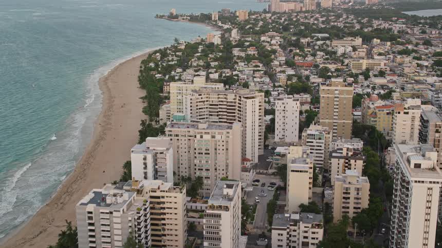 A city with several tall buildings next to a beach and there are some waves breaking on the shore
