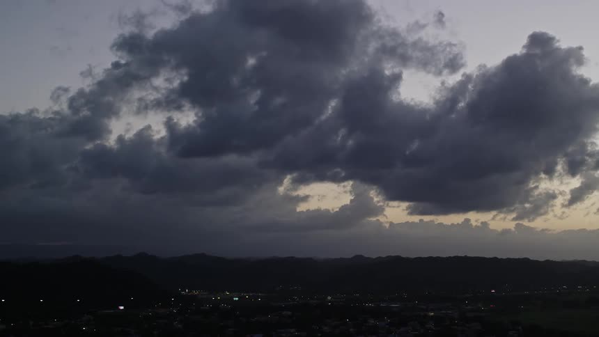 A region with a small town and in the background there are mountains and there are big gray clouds in the sky