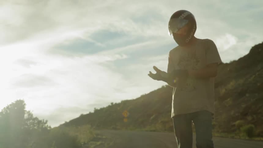 A man wearing a motorcycle helmet is standing on the side of the road adjusting his gloves
