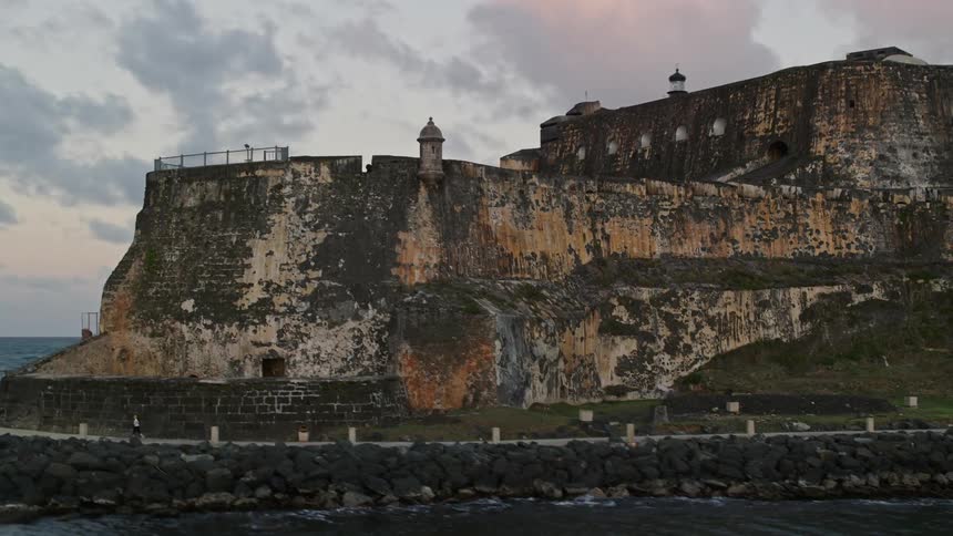 A large and old fort sits on a headland coast near a city