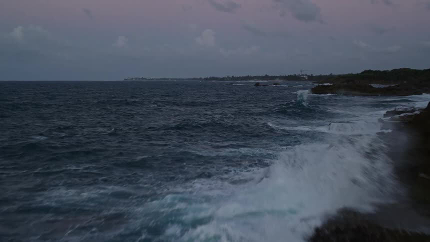 Waves crash onto coast near trees under a red tinted cloudy sky
