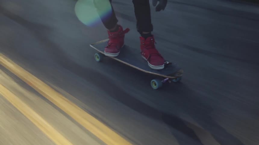 A skateboarder wearing a pink helmet rides down a mountain road at a fast speed