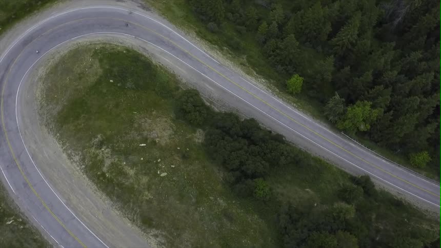 Two people ride down a windy mountain road