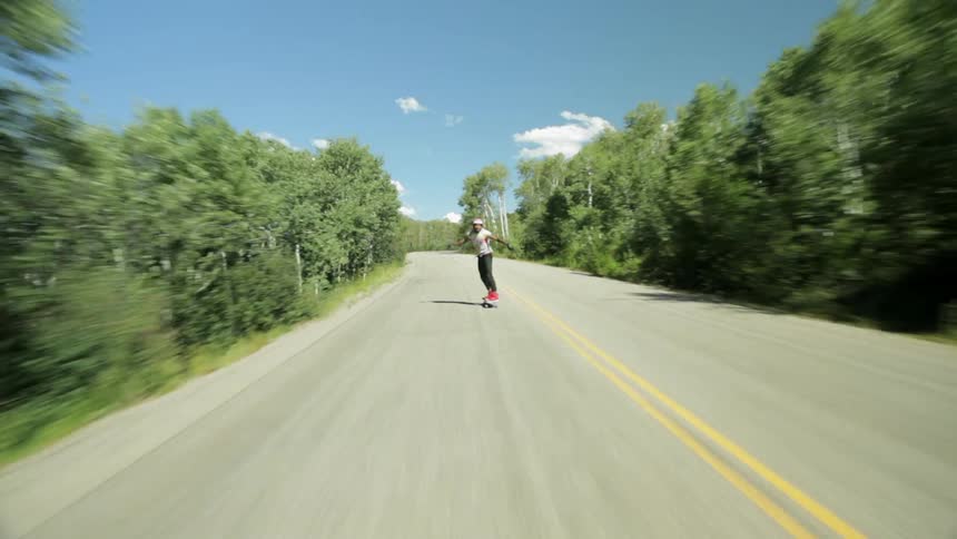 A skateboarder rides down a mountain road at a fast speed