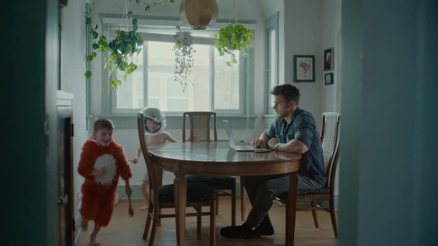A father sits in the kitchen while his boys run around playfully