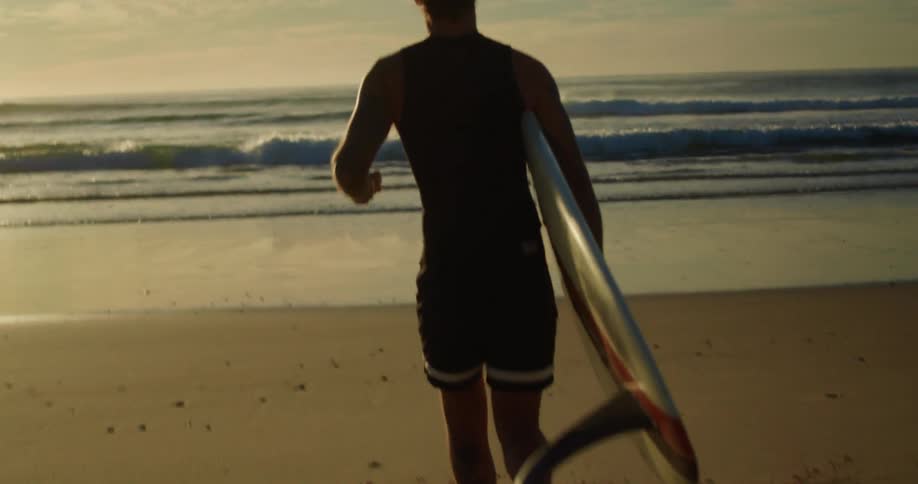 A man jugging towards the sea with a surfboard at sunset
