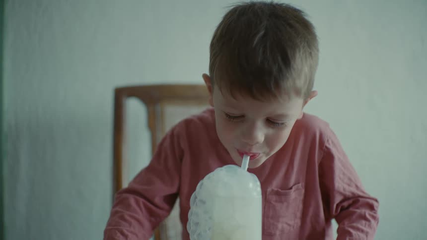 Boy blows air bubble on a glass of milk with a straw
