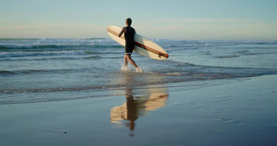 Surfer with his long board runs as he enters the sea