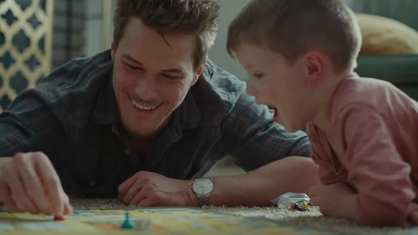Father lying on the carpet with his little son playing board game with dice