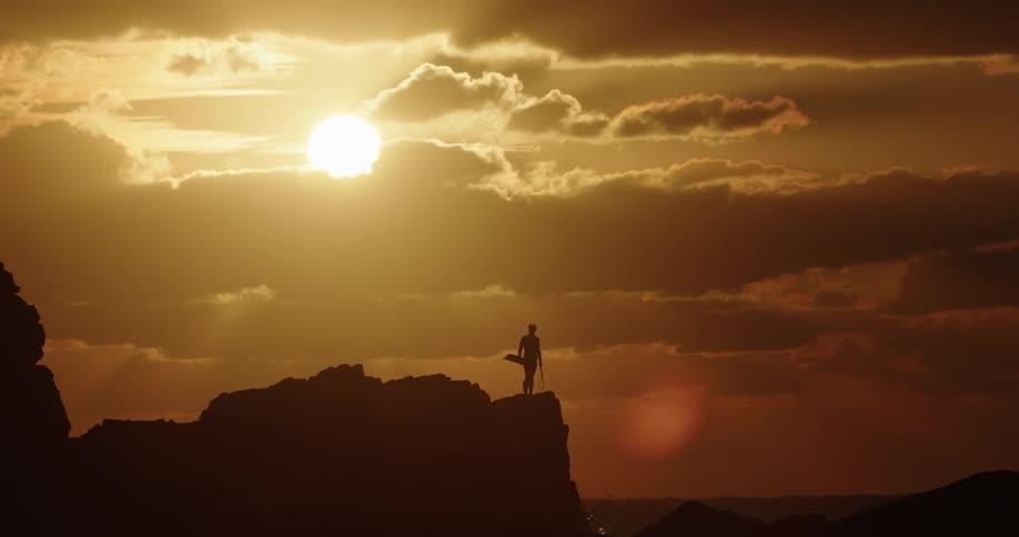 Silhouette of a man on a cliff by the sea on a day with a reddish sky and a strong sun