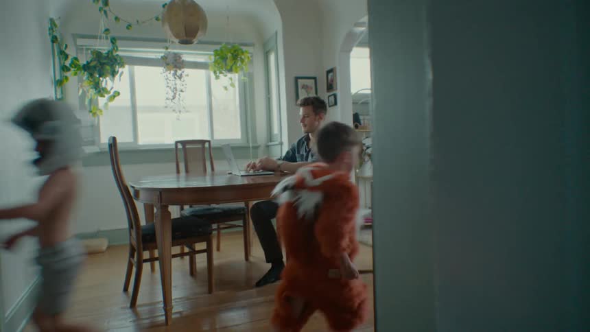 A father attempts to work at a dining room table as his kids play