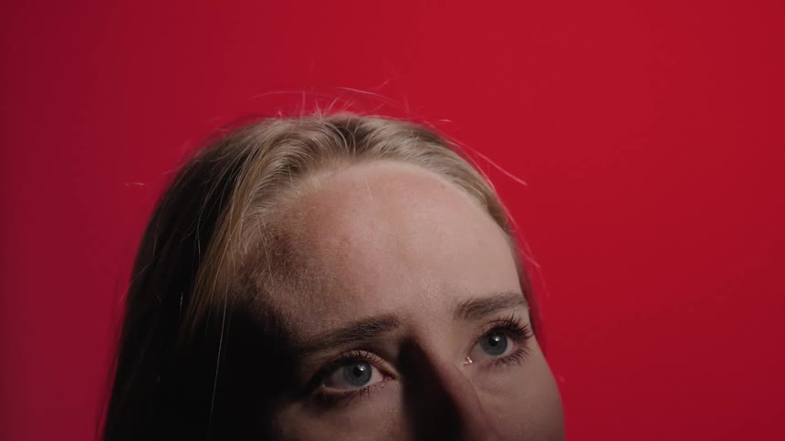 A woman gazes while being in front of a red background