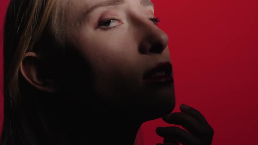 Blonde woman turns her head to look against a red background