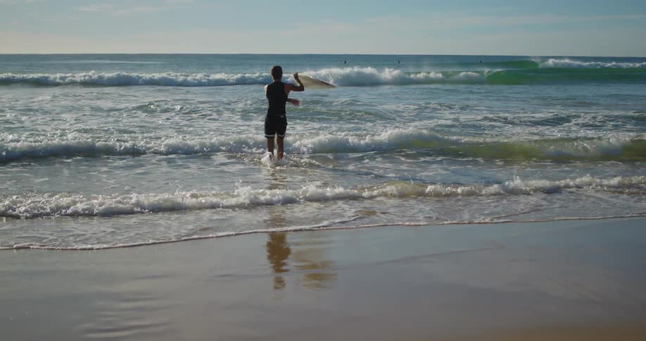 Man with his back going into the sea with his surfboard