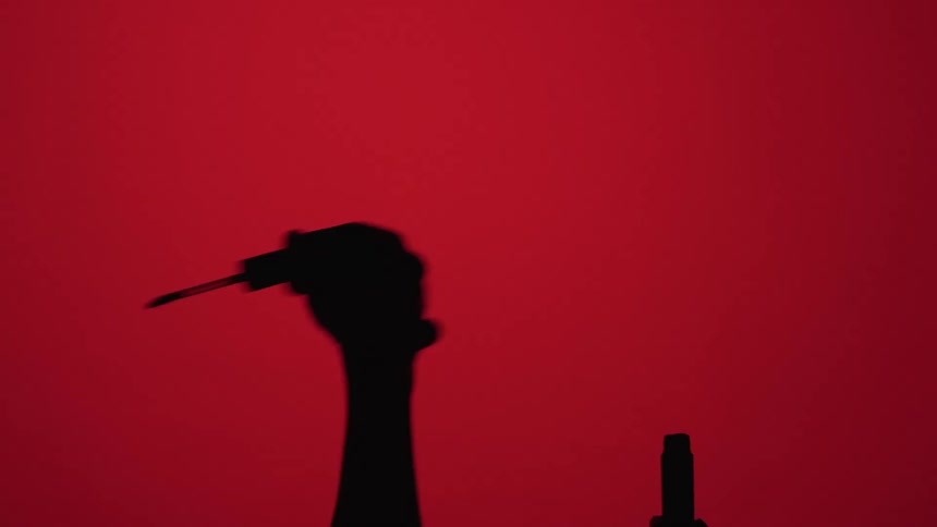 Silhouette of a persons hands opening a lip gloss on a red background