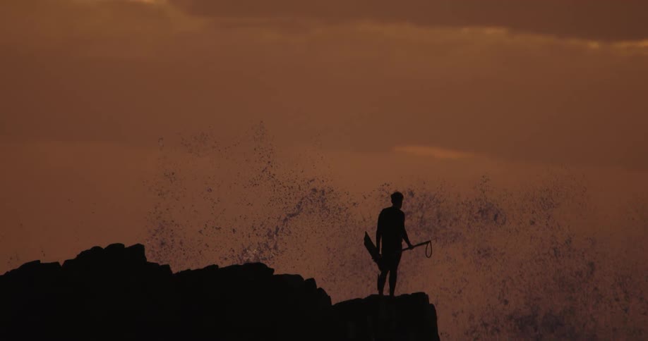 Silhouette of a man on a cliff overlooking the sea on a day with a reddish sky