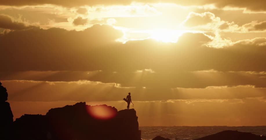 Silhouette of a person on the cliff on the coast facing the sea with the strong late afternoon sun