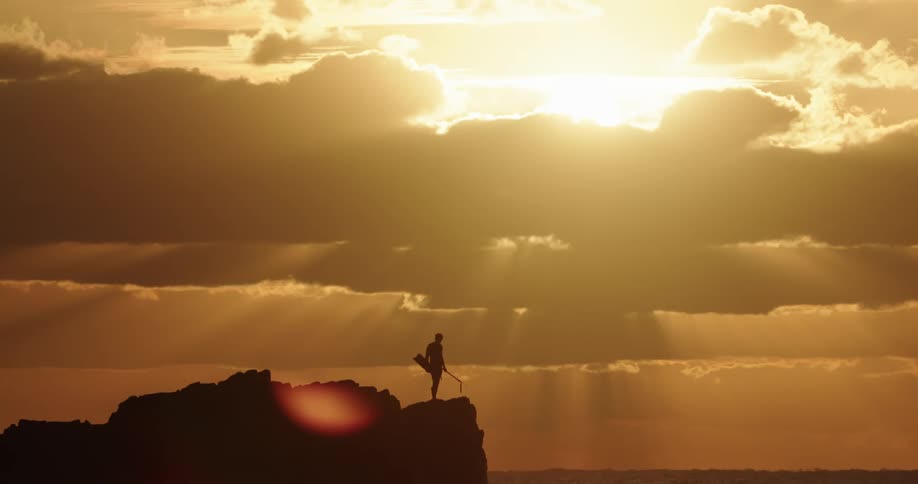 The silhouette of a person can be seen standing on a cliff overlooking the ocean