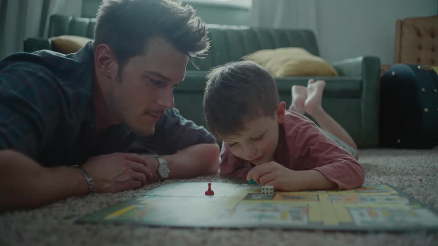 Father lying with his son on the rug and playing a board game
