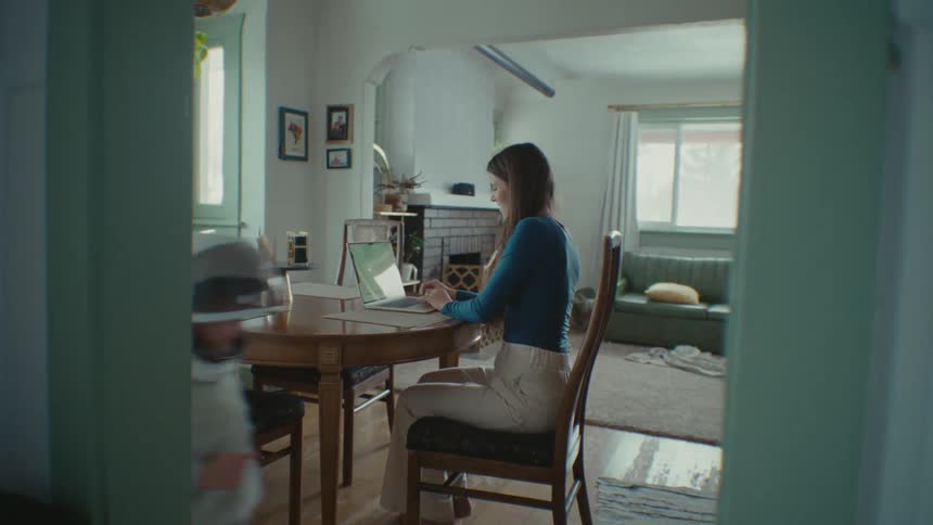 A woman types on a laptop while her children play