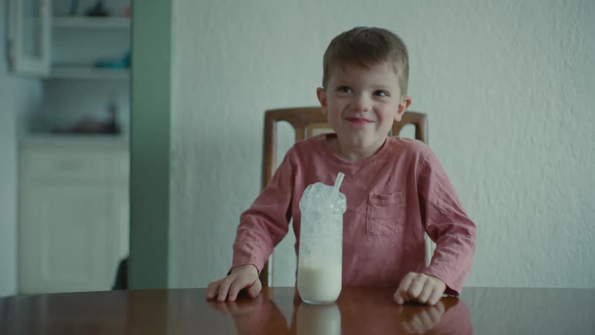 A kid in a pink shirt blows bubbles into his milk